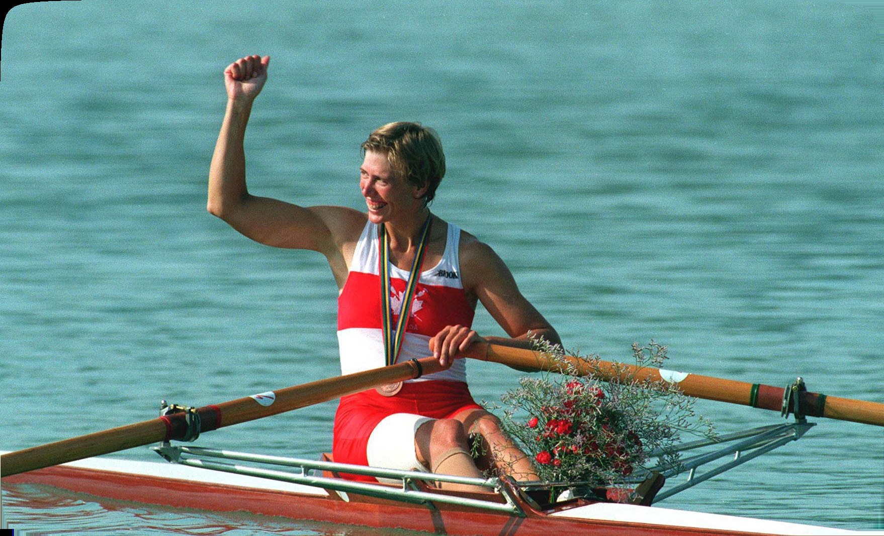 Silken Laumann raising a fist in her scull at Barcelona 1992, bronze medal around her neck and her right leg bandaged